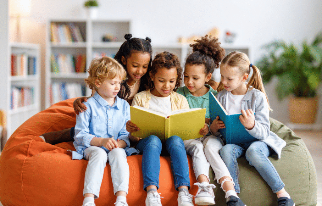 Group of diverse children sitting together on a bean bag, reading books and learning about financial literacy for kids in a classroom or library setting.